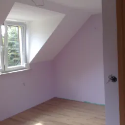 Pokój na poddaszu z wykończonymi ścianami w odcieniu liliowym, nową drewnianą podłogą i oknem dachowym z widokiem na drzewa, widoczne przewody elektryczne przy drzwiach.